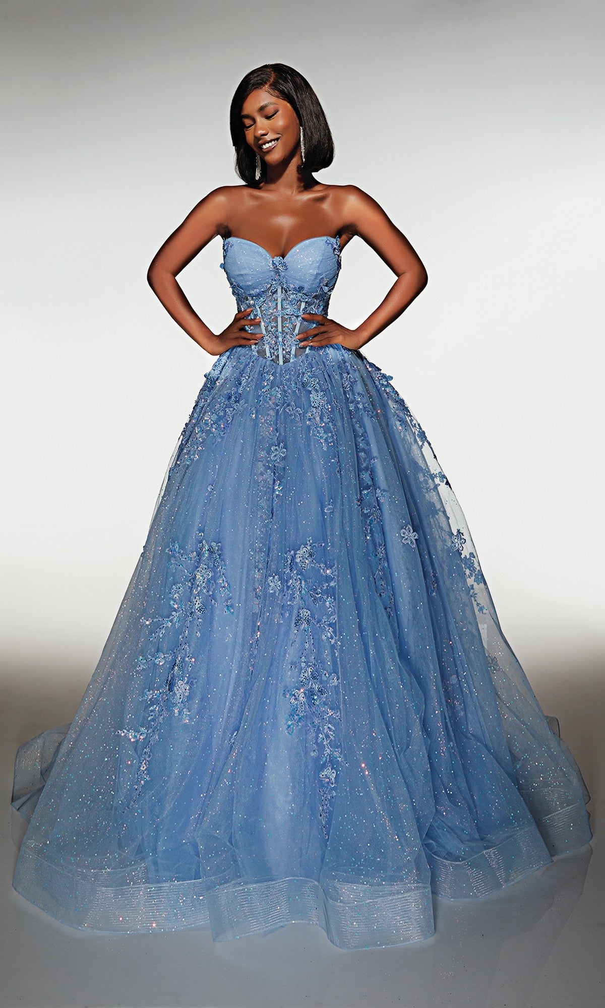 A woman wearing the Long Prom Dress: Alyce 62163 in periwinkle, featuring a strapless embellished corset bodice with floral details, stands with hands on hips and smiles against a plain background.